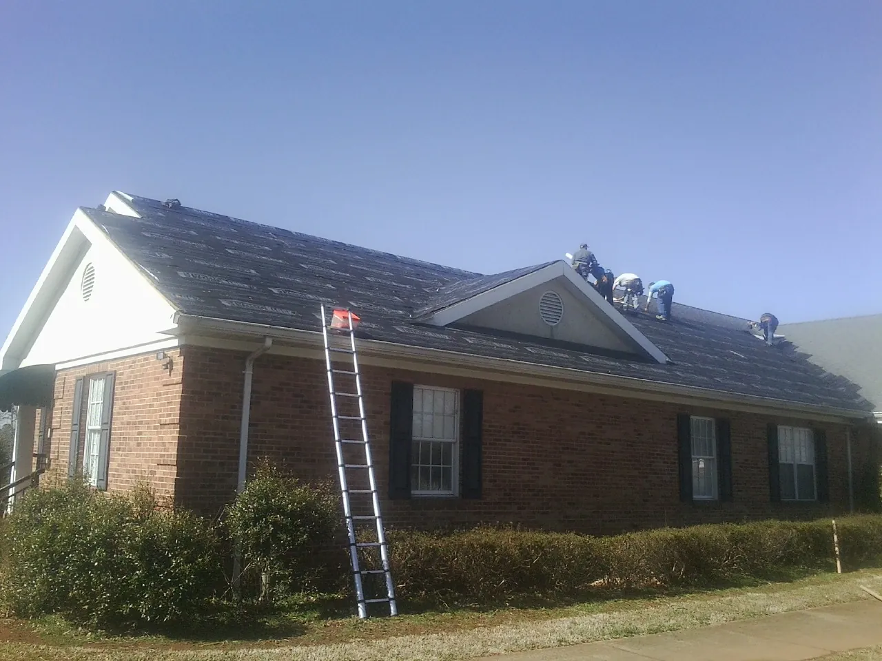 Crew tearing shingles off a brick ranch roof with a ladder set — Emergency Roof Repair work by our crew in West Nottingham