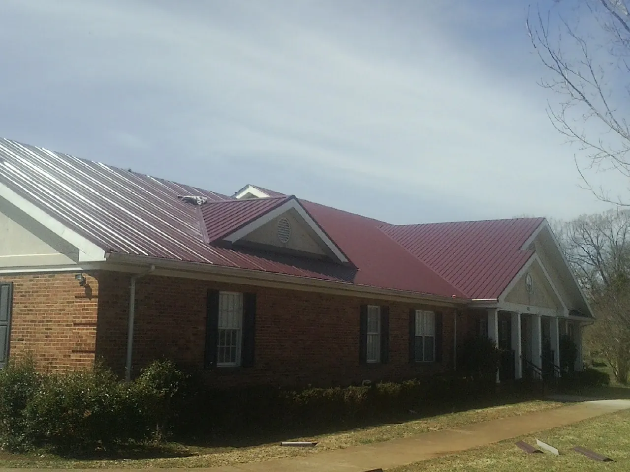 Red metal roof with gabled entries on a long brick building, from a Hail Damage Roof Repair job in West Nottingham