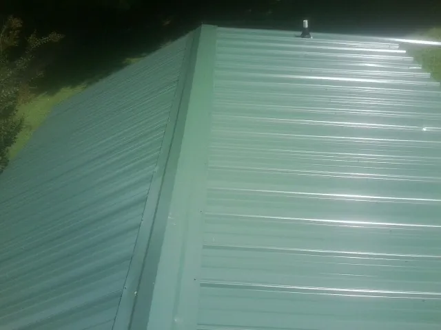 New green metal panels meeting at the ridge of a roof — Flat Roof Repair work by our crew in West Nottingham