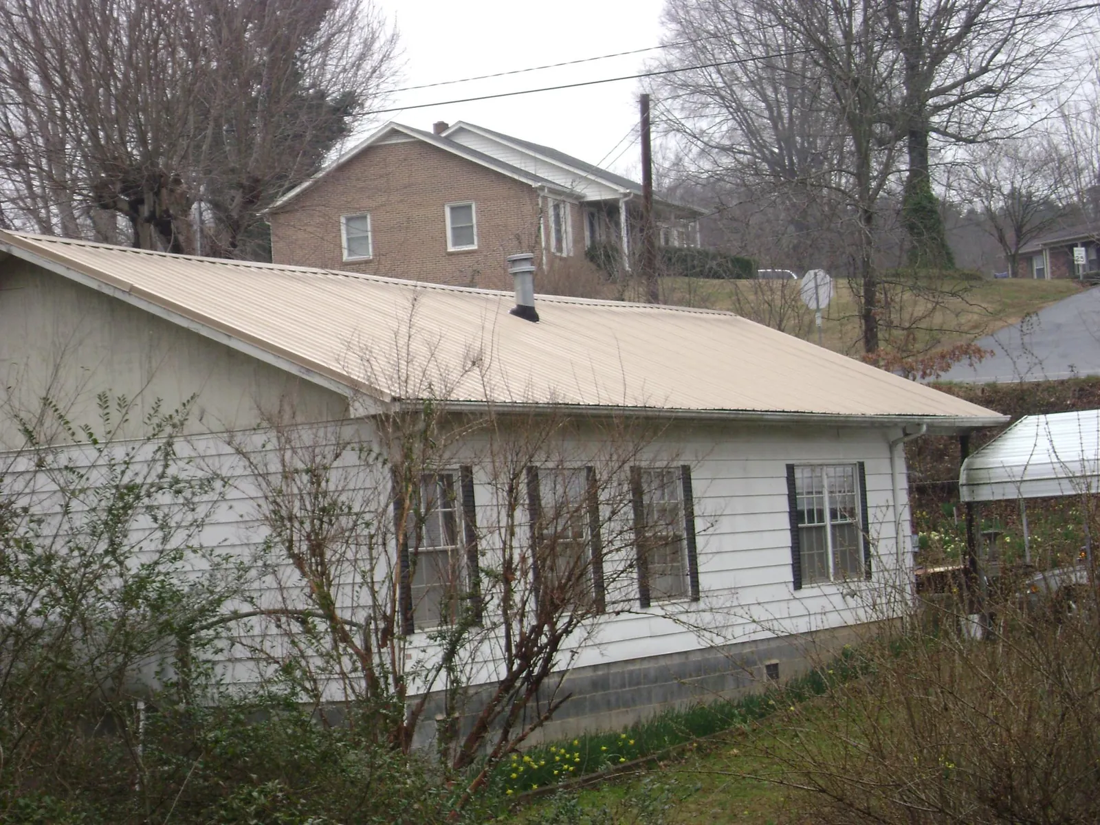 Tan metal roof on a white sided house set into a hillside — Commercial Roofing by Roofing Brothers in West Nottingham